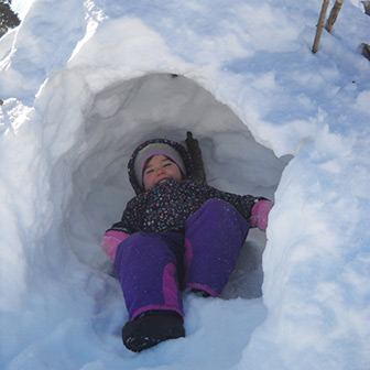 child grinning in a snow fort